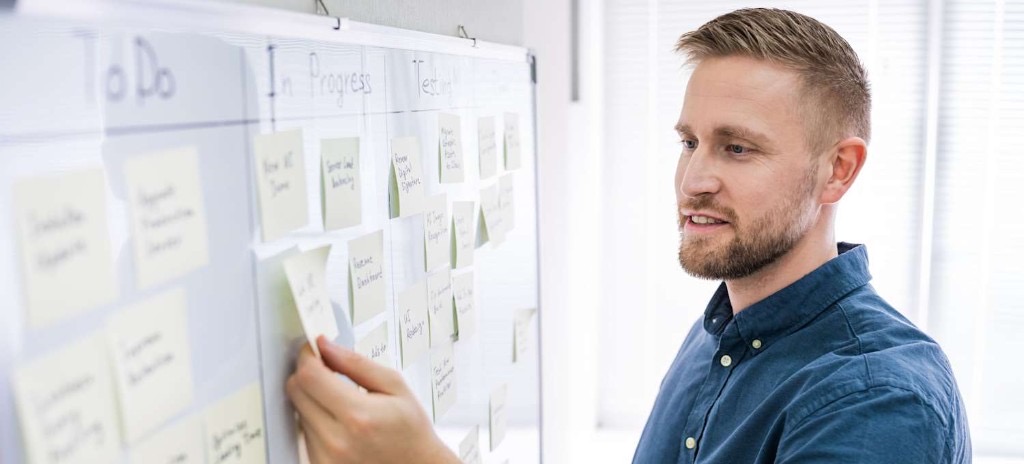 Persona colocando nota adhesiva en tablero Kanban físico con columnas de reposición