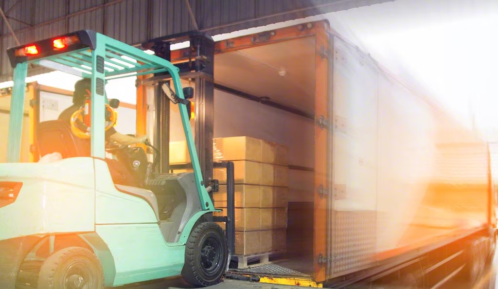 Montacargas carga un pallet de cajas al remolque abierto en andén de transferencia